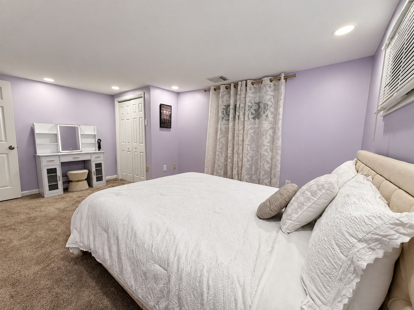 A bedroom with a bed, a vanity with a mirror, a door, and a window with blinds.