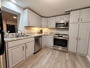 A modern kitchen with white cabinetry, stainless steel appliances, and a marble countertop. - Willow Terrace House (Mechanicsburg)
