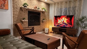 A living room with a brick wall, a flat-screen TV, leather sofas, wooden coffee table, and a fireplace. - Willow Terrace House (Mechanicsburg)