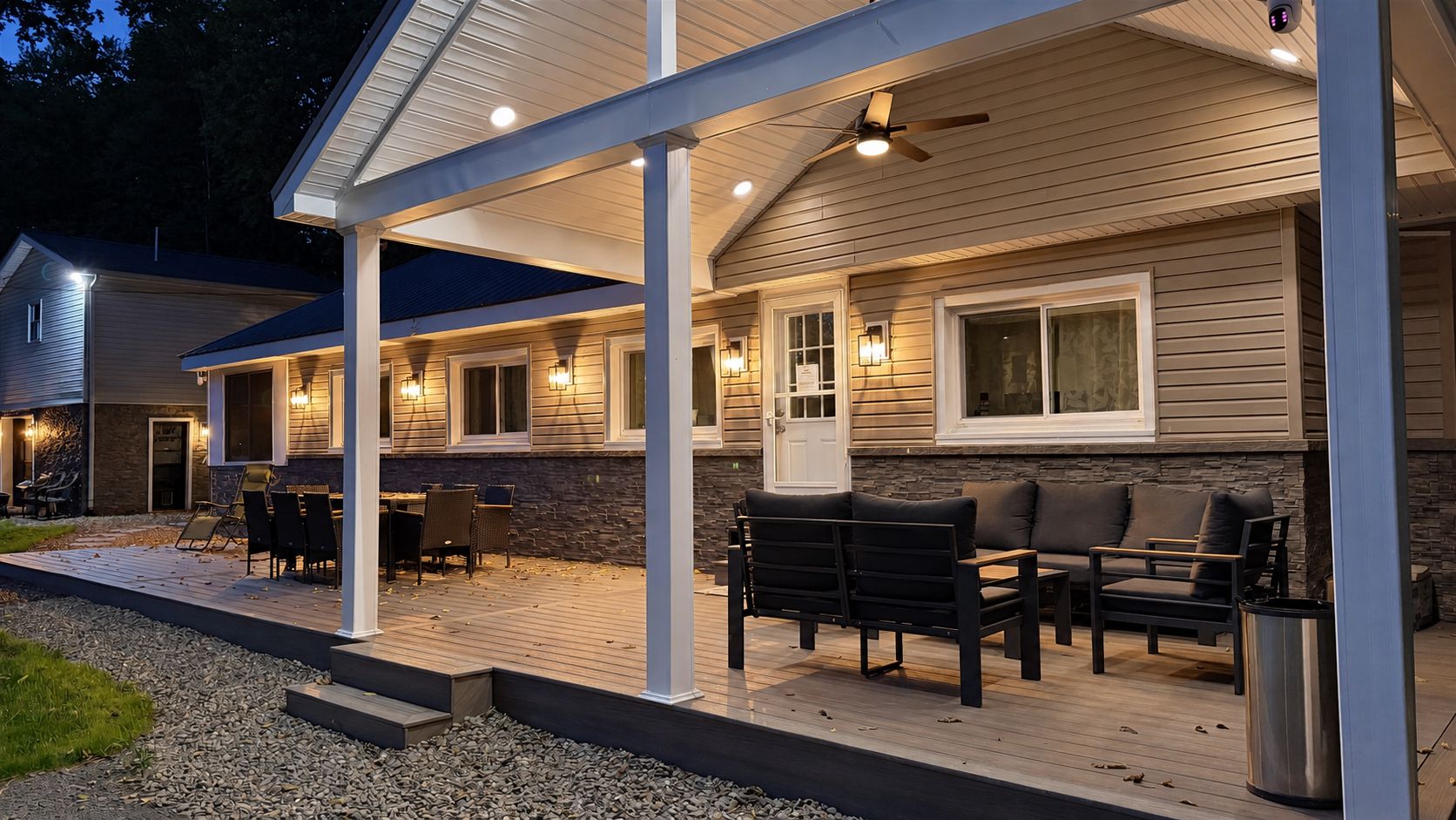 A covered outdoor patio with seating, a ceiling fan, and wall-mounted lights.