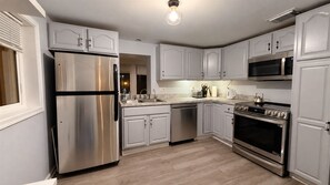 A modern kitchen with stainless steel appliances, white cabinetry, and a wooden floor. - Willow Terrace House (Mechanicsburg)