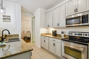 Una cocina moderna con armarios blancos, encimera de granito, horno de acero inoxidable y microondas.