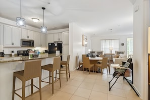 A modern kitchen with white cabinets, a black refrigerator, and a dining area with a table and chairs. - 3BR Vista Cay Condo Near Universal (Orlando)