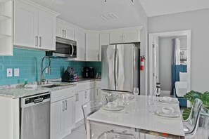A modern kitchen with white cabinets, a stainless steel refrigerator, a microwave, and a dishwasher. - Modern 2-bedroom Enclave Condo Retreat (Orlando)