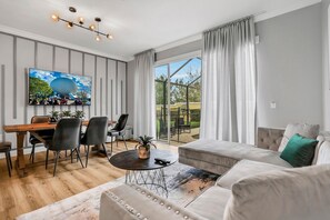 A modern living room with a dining area, large windows, and a view of the outdoors. - 3bd/3ba Windsor Hills, 10 min to Disney (Kissimmee)