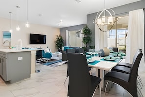 Un salon moderne comprenant un coin repas, une cuisine et une grande fenêtre laissant entrer la lumière naturelle.