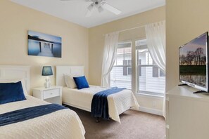 Un dormitorio con dos camas, ventilador de techo, televisión y ventana con cortinas.