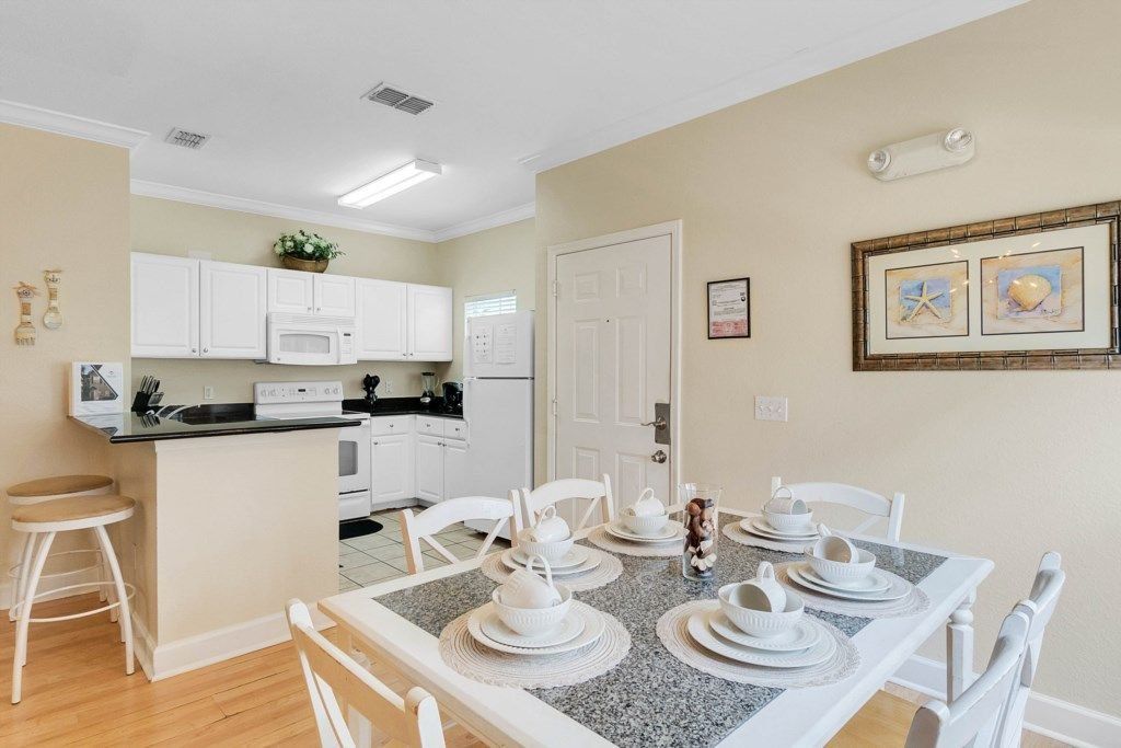 A modern kitchen with white cabinets, a central island, and a dining area set for four with white chairs and a granite table.