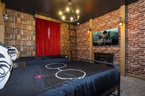 Une pièce avec un mur en briques, une bibliothèque, un téléviseur diffusant un film de « Harry Potter », et deux lits ornés de motifs circulaires.