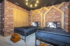 Ein Zimmer mit zwei Metallbetten, einer Ziegelwand, einer Holztür und einem Kronleuchter.