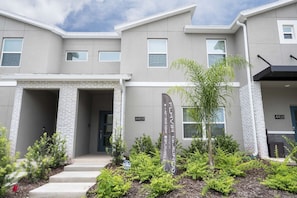 A modern building with a grey facade, a brick entrance, and a sign for 'FLAVIA SUEROS'. - 4BR Storey Lake Townhome, Private Pool (Kissimmee)