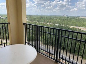 Un balcon avec une table blanche et une vue sur une route et la verdure.