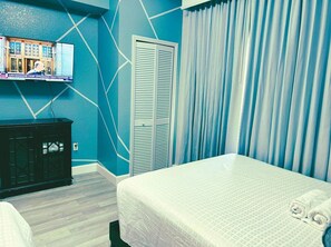Une chambre d’hôtel comprenant un lit, une armoire, un téléviseur fixé au mur et une fenêtre avec des rideaux.