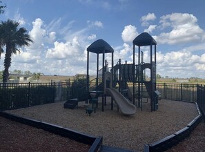 A playground with two covered play structures and a slide, surrounded by a fence and gravel ground. - Lake Buena Vista Resort - 2BR Condo (Orlando)