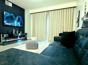A modern living room with a flat-screen TV, a fireplace, a dark sofa, and a large window with curtains. - Lake Buena Vista Resort - 2BR Condo (Orlando)