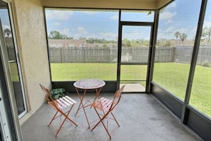 A covered patio with a table and chairs, a view of a fenced yard, and a building in the background. - 4BR Montego Bay Villa Near Disney (Kissimmee)