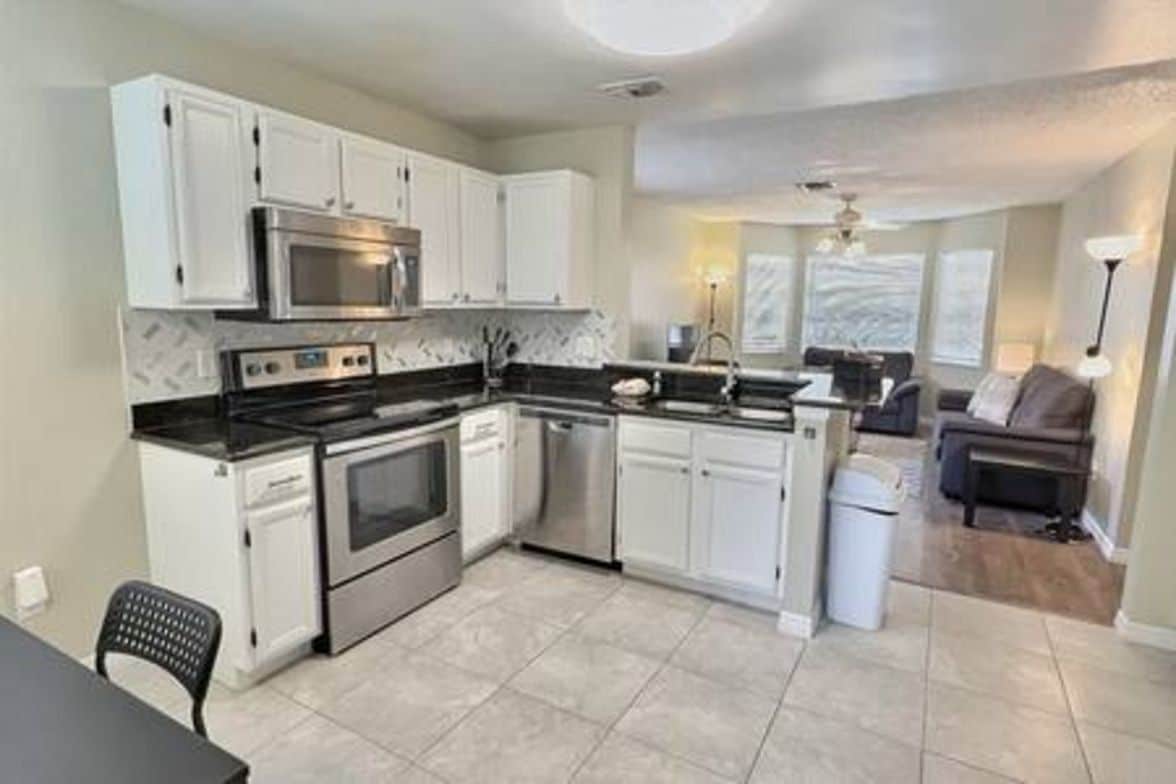 A compact kitchen with white cabinets, a microwave, stove, and dishwasher.