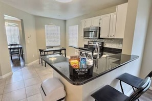 A kitchen with a black countertop, white cabinets, a microwave, and a welcome sign. - 4BR Montego Bay Villa Near Disney (Kissimmee)