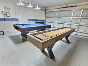 A billiards table and a foosball table in a room with a garage door and a clock on the wall. - 4BR Lake Berkley Home, Heated Pool (Kissimmee)