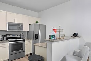 Eine moderne Küche mit weißen Schränken, Edelstahlgeräten, einer Mikrowelle, einem Backofen, einem Kühlschrank und einer kleinen Kochinsel mit Spüle und Arbeitsplatte.