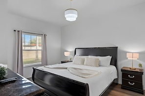 A bedroom with a bed, bedside tables, a window with blinds, and a hanging light fixture. - Modern 3BR Villa Near Disney & Resort Access (Kissimmee)