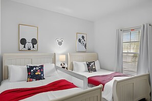 Ein Hotelzimmer mit zwei Betten, weißen Kopfteilen und Kissen mit Mickey Mouse Motiv.