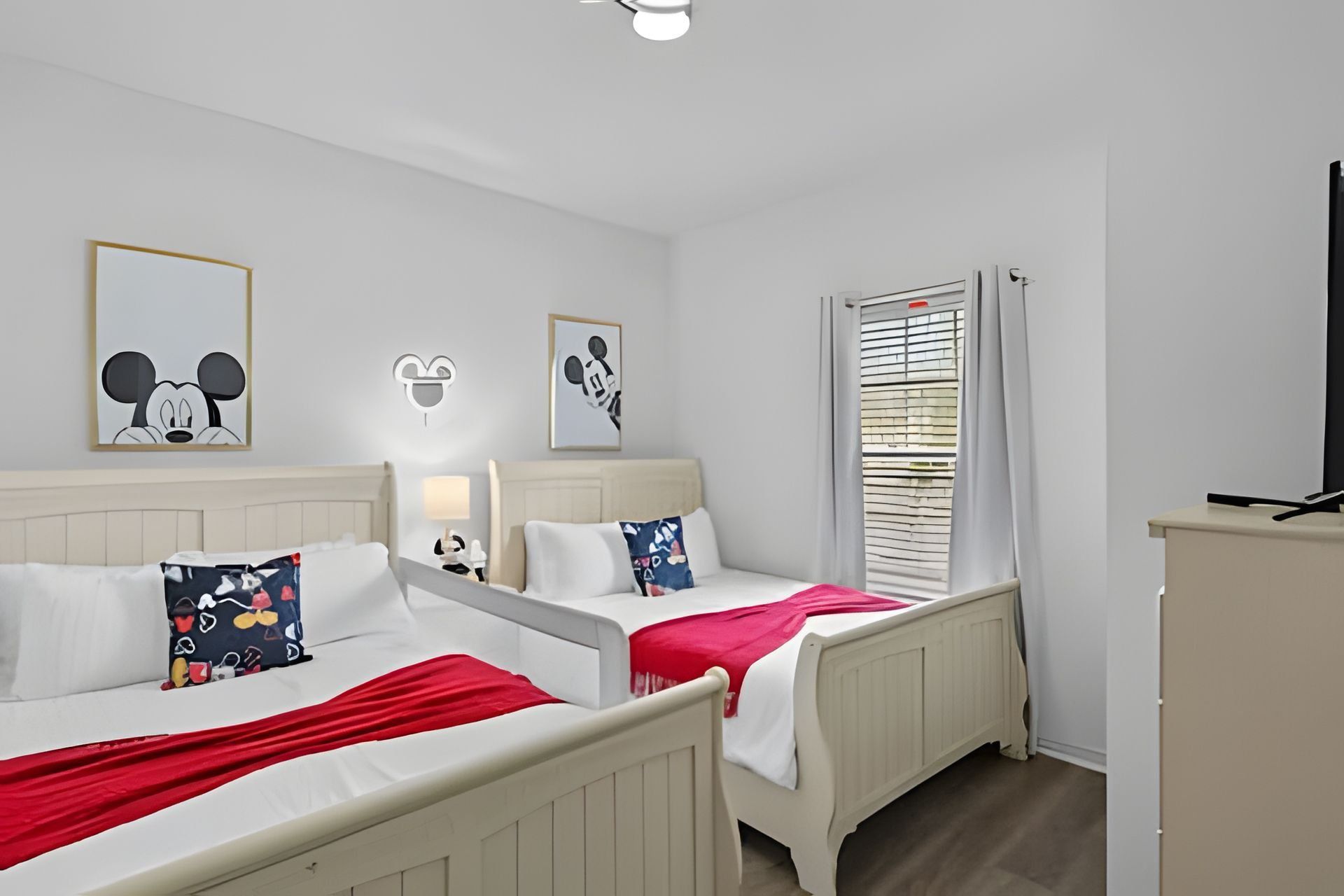 Habitación de hotel con dos camas, televisión, escritorio y decoración temática de Mickey Mouse.