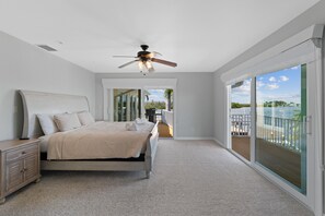 A bedroom with a bed, a nightstand, a ceiling fan, and a view of a balcony with a railing. - Lured Away (Fort Myers Beach)