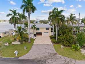 A residential property with a paved driveway, palm trees, and a view of the water. - Lured Away (Fort Myers Beach)