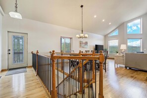 A spacious living area with a wooden staircase, a chandelier, and large windows providing natural light. - Timberline Hideout! Secluded Mtn Escape w Hot Tub (Woodland Park)