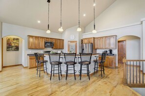 A spacious kitchen with wooden cabinets, a central island with bar stools, a refrigerator, and a microwave. - Timberline Hideout! Secluded Mtn Escape w Hot Tub (Woodland Park)