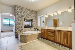 Une salle de bain avec un mur d’accent en pierre, une grande baignoire, des meubles en bois et un grand miroir avec éclairage intégré.