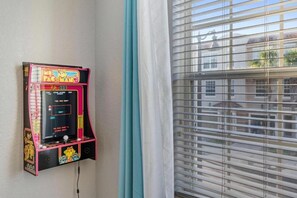 A Pac-Man arcade machine mounted on a wall next to a window with blinds. - Modern 3BR Vista Cay Townhome (Orlando)