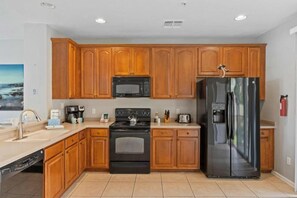 Une cuisine avec des meubles de rangement en bois, une cuisinière noire, un four à micro-ondes, un réfrigérateur et un lave-vaisselle.