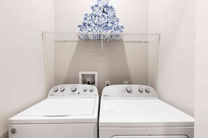 A laundry room with two white Whirlpool washers and dryers, a metal drying rack with folded towels, and a small door leading to a utility room. - Orlando 4BR Townhome Summerville Resort (Kissimmee)