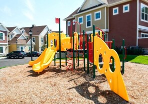 A playground with a yellow slide and climbing structures, set against a backdrop of residential buildings. - Orlando 4BR Townhome Summerville Resort (Kissimmee)