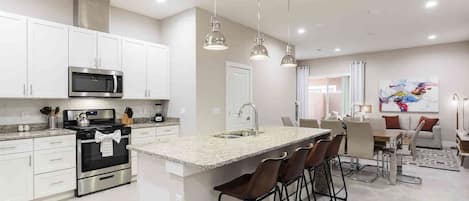 A modern kitchen with white cabinets, stainless steel appliances, and a central island with bar stools.