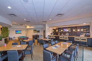 A well-lit indoor space with multiple tables and chairs, a pool table, a bar area with a TV, and a large screen displaying a sports game. - Encantada Resort Condo w/ Pool & Lake View (Kissimmee)