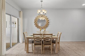 A dining area with a round mirror, chandelier, and six wooden chairs with cushions. - Storey Lake 4BR Townhome - 10 min to Disney (Kissimmee)