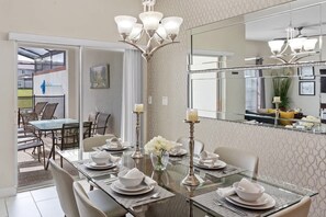 A dining area with a glass table set for four, a chandelier, and a large mirror reflecting the room. - Storey Lake 4BR Home - Private Pool (Kissimmee)