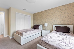 A bedroom with two beds, a white headboard, a nightstand with a lamp, and a patterned wallpaper. - Storey Lake 4BR Home - Private Pool (Kissimmee)