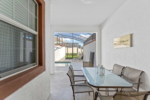 A dining area with a glass table and metal chairs, a view of a swimming pool, and a framed quote on the wall. - Storey Lake 4BR Home - Private Pool (Kissimmee)