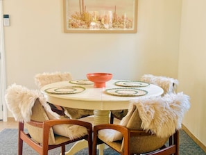 A round dining table with a central orange bowl, surrounded by chairs with fluffy, fur-like armrests. - Pixie and Orchard Cottages - Sleeps 7 (Ojai)