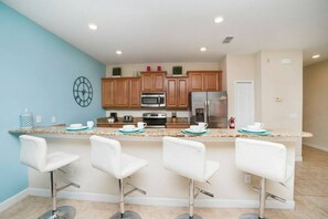 A modern kitchen with a central island, bar stools, and stainless steel appliances. - 4BR Townhome w/ Private Pool at Paradise Palms (Kissimmee)