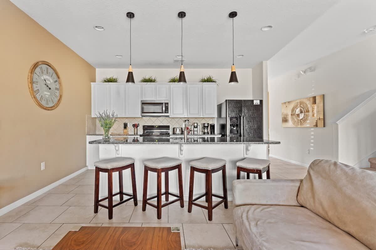 Una cocina moderna con armarios blancos, una isla central con taburetes altos e iluminación colgante.