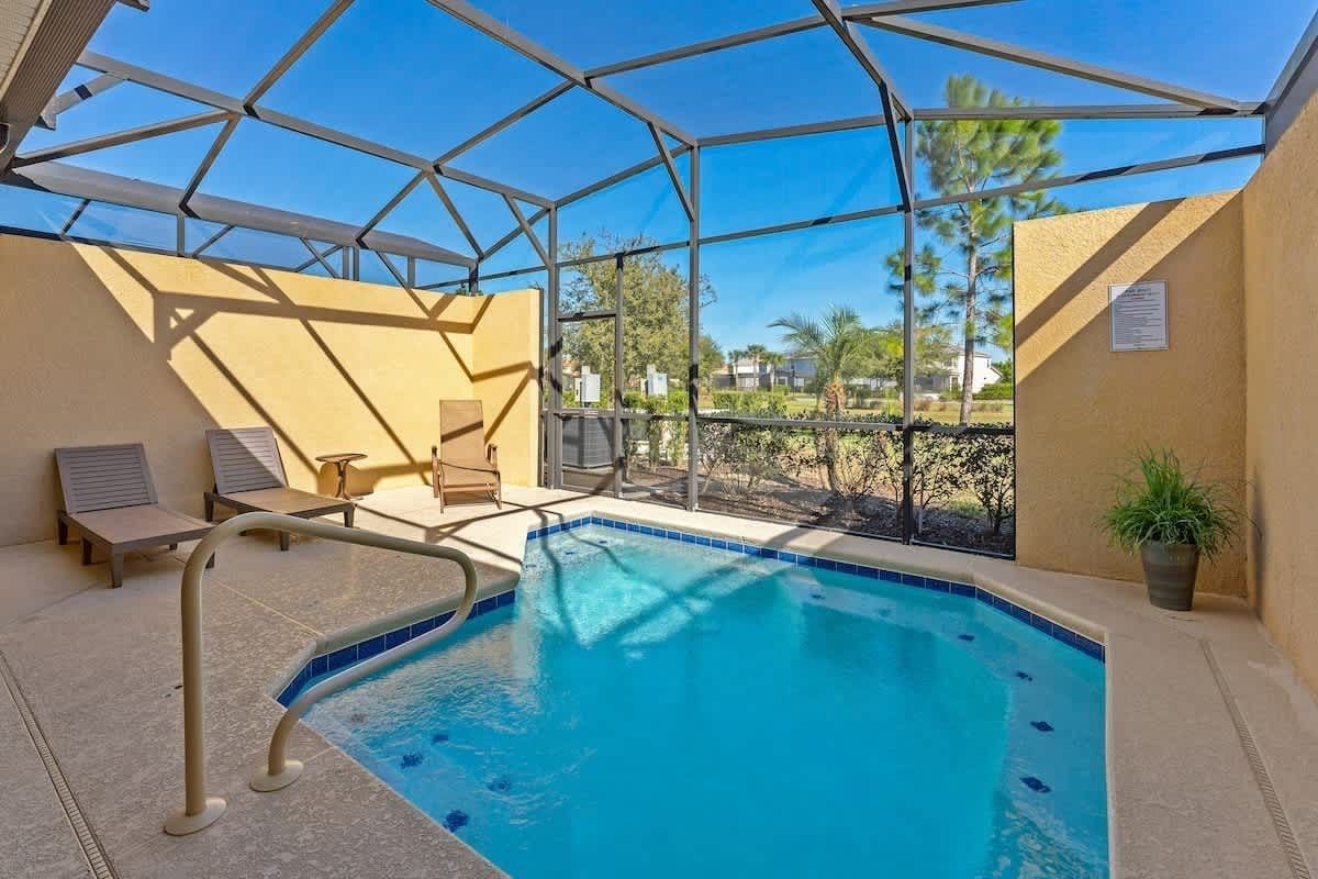 A swimming pool with a glass enclosure, lounge chairs, and a view of the surrounding landscape.