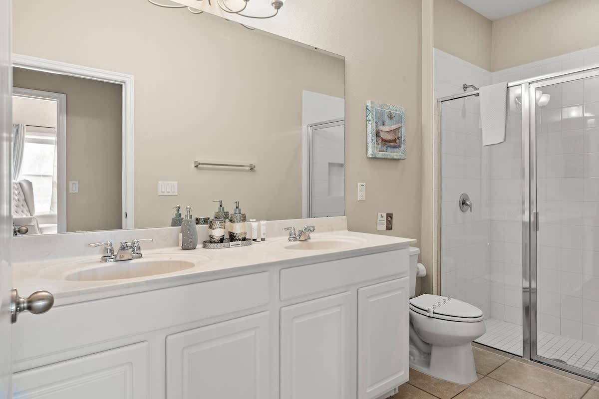 A bathroom with a double sink vanity, a toilet, a glass shower enclosure, and a large mirror.