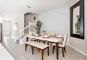 A dining area with a white table set for four, a bench, and a staircase with a railing. - Solterra 4BR Home w/ Private Pool (Davenport)