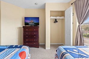 A bedroom with two beds, a dresser, a television displaying a Disney scene, a window with curtains, and a door leading to a closet. - 3BR Home at Seven Dwarfs Resort w/ Pool (Kissimmee)