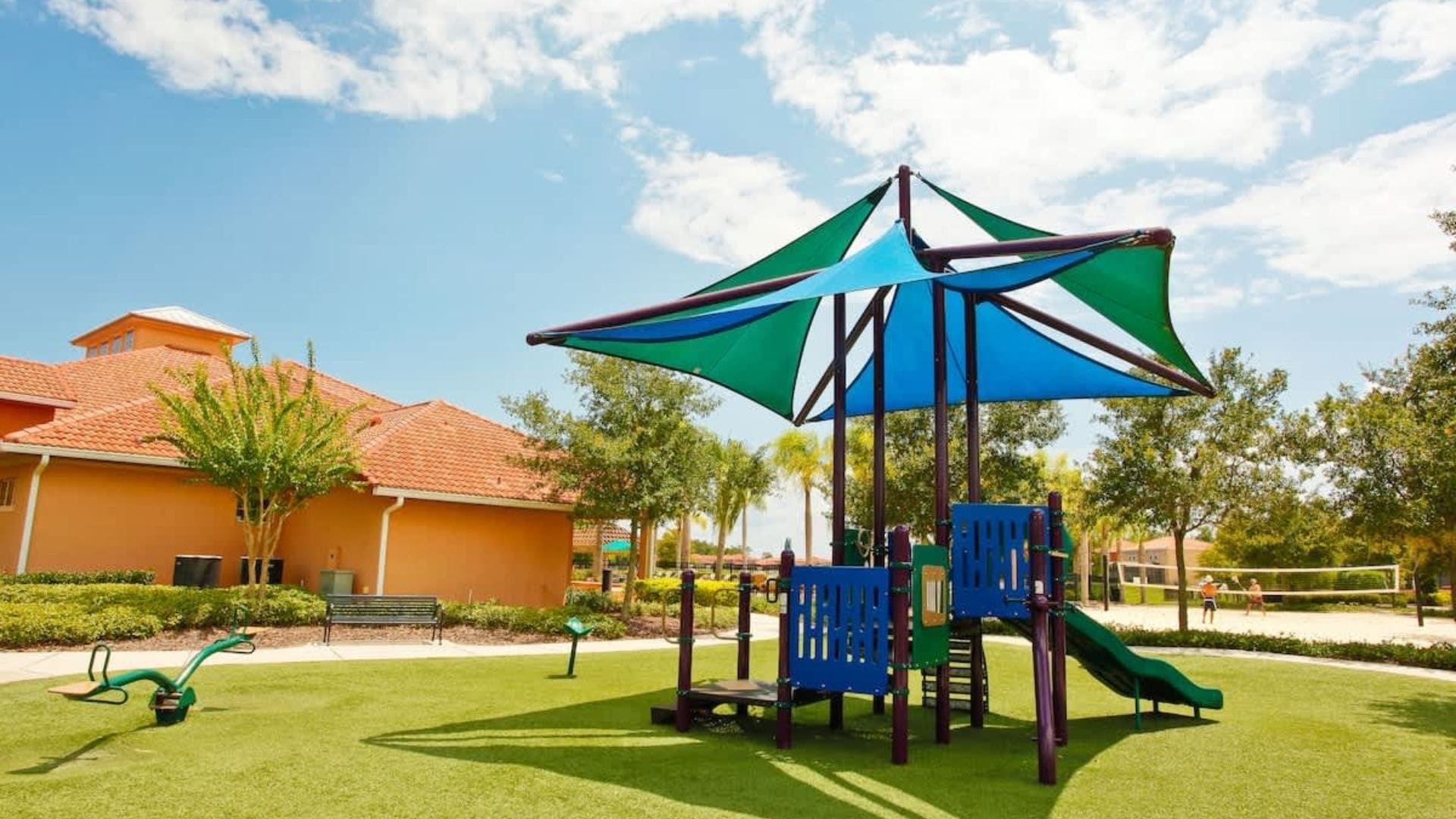 A playground with a climbing structure and slides, surrounded by a well-maintained lawn and a building with a red-tiled roof.